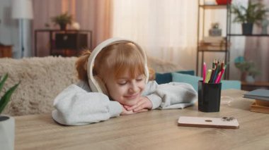 Masada uzanmış kulaklıklı bir sesli kitabı dinleyen genç bir kız heyecanla tepki veriyor, sürpriz. Beyaz çocuk neşeyle gülümsüyor, hikayede sırada ne olduğunu merak ediyor, evde maceranın tadını çıkarıyor.