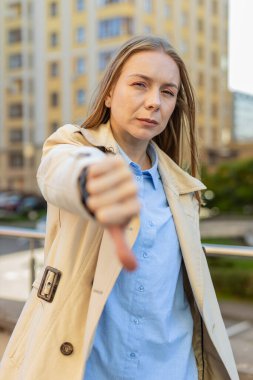 Hoşlanmamak. Kafkasyalı yetişkin bir iş kadınının baş parmağıyla işaret hareketi göstermesi hoşnutsuzluğunu dile getirmesi, tatminsiz kötü iş yapması, açık havada hata yapması. Şehir caddesinde ceketli mutsuz bir kız..