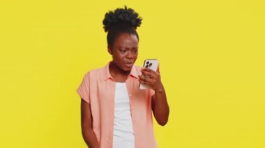 Üzgün Afrikalı Amerikalı kadın akıllı telefon daktilo oyunu kullanıyor. Ani piyango yüzünden kaybediyor. Kötü şans kaybı kötü haber. Mutsuz siyah kız sarı arka planda izole edilmiş.