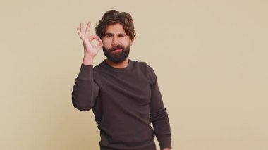 Lübnanlı uzun kollu neşeli adam kameraya olumlu geri bildirim jesti göstererek olumlu bir işaret vermiş gibi bakıyor. Bej arka planda yakışıklı bir adam. İnsanlar samimi duygular