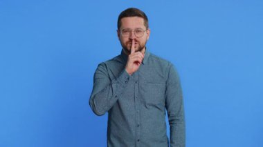 Sessiz olun lütfen. Gözlüklü, orta yaşlı beyaz bir adam işaret parmağını dudaklarına bastırıyor. Sessiz jest işareti yapıyor. Gizli saklı konuşma, gizli mahremiyet. Mavi arka plandaki adam