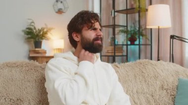 Kapüşonlu üzgün genç adam boğaz ağrısı çekiyor. Ağrılı boyun ve kaşları çatık, tiroid bozuklukları boğaz ağrısı, bademcik iltihabı. İspanyol erkek, sınıftaki kanepede oturuyor..