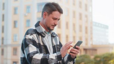 Şehir merkezinde online şok yaşayan erkek turist kazanan cep telefonu kullanan heyecanlı orta yaşlı adam zafer başarısını kutlamak için akıllı telefon bahsini kazandı. Şehir sokağında duran adam.