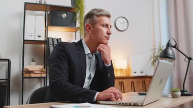 Takım elbiseli bir işadamı ofis masasında önemli bir yaratıcı proje çalışması kararı düşünüyor. Kendine güvenen erkek yönetici serbest çalışan adam dizüstü bilgisayardaki analitik raporlara bakmakla meşgul..