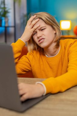 Beyaz çocuk evde bilgisayarında zor bir video oyunu oynarken hayal kırıklığına uğradı. Sinirli bir şekilde klavyeye vuruyor, kaybettiği için üzgün bir şekilde masa masa oturuyor, hayal kırıklığını ifade ediyor.