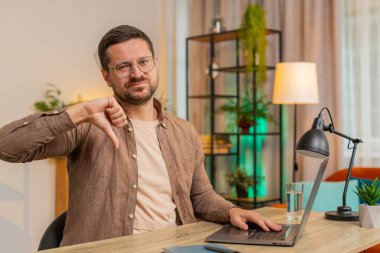 Hoşlanmamak. Mutsuz bir adam dizüstü bilgisayar kullanıyor ve işaret dilini gösteriyor. Memnuniyetsizliğini dile getiriyor. İç işlerindeki kötü işleri tasvip etmiyor. Masadaki serbest çalışan genç adam memnun değil..