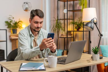 Ofiste gülümseyen cep telefonuyla masada oturan mutlu beyaz bir adam. Serbest çalışan biri, internetten akıllı telefon sosyal medya uygulamalarından mesaj yolluyor. Yaşam biçimi.