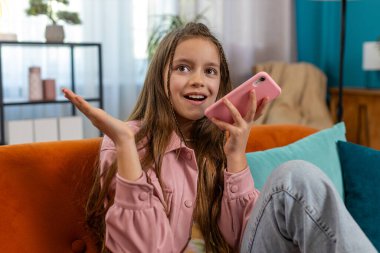 Mutlu kız çocuğu arkadaşlarıyla çevrimiçi telefon görüşmesi yapıyor. Mobil hoparlörlerden hoşlanan beyaz kadın portresi. Oturma odasında kanepede sohbet ediyorlar..