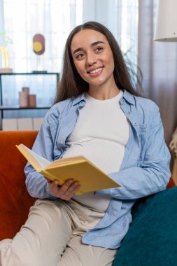 Hamile kadın kitap okuyor. Evdeki rahat koltukta rahatlıyor. Müstakbel anne güzel kız çocuk bakımı rehberini okuyup doğum öncesi hazırlıyor. Rahatlama ve hamilelik kavramı. Dikey