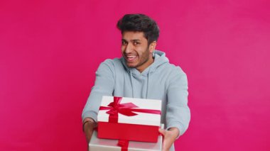Doğum günü hediyelerini sunan pozitif gülümseyen Hintli adam ellerini uzatıyor, hediye paketine sarılmış kariyer ikramiyesi teklif ediyor, parti promosyon indirimi satışını kutluyor. Pembe arka planda izole edilmiş Arap adam.