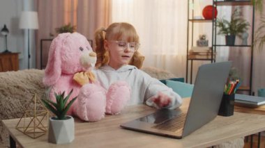 Genç liseli kız laptopun yanında pelüş tavşan oyuncağıyla oturmuş evde eğitici bir video izliyor. Kafkasyalı çocuk videoyu neşe ve merakla tavşan arkadaşına materyali açıklamak için durdurdu