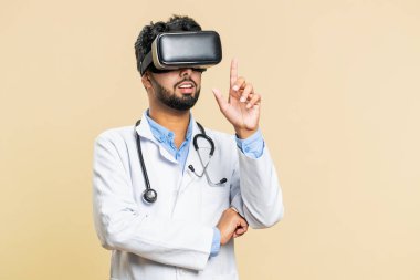 Heyecanlı Hintli doktor kardiyolog kulaklık uygulaması kullanarak sanal gerçeklik 360 videosu izliyor. VR gözlüklü, bej arka planda Arap eczacı. Geleceğin tıp teknolojisi.
