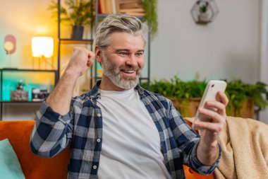 Heyecanlı, olgun bir adamın elinde akıllı telefon tutarak online bahis oyununun kazanmasıyla hayrete düşen iyi haberleri okumasına şaşırdım. Mutlu gri saçlı, beyaz saçlı, yaşlı bir adam. Ekrana bakıyor. Memleketteki zafer başarısından çok memnun..