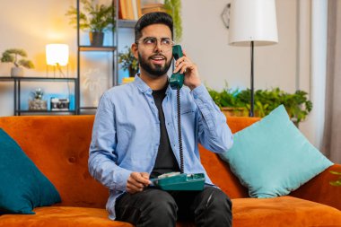 Evdeki rahat koltukta oturan arkadaşlarıyla telefon konuşması yapan genç Hintli adamın portresi. Mutlu, heyecanlı İspanyol adam 90 'lardan kalma eski moda telefonlardan keyif alıyor.