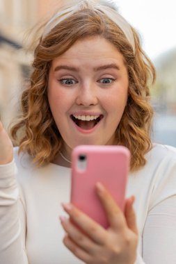 Aman Tanrım. Vay canına. Heyecanlı, mutlu, neşeli, uzun elbiseli genç kadın akıllı telefon kullanıyor, kutlama yapıyor, dışarıda iyi haberler kazanıyor. Şehir caddesinde cep telefonlu bir kız yürüyor..