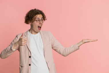 Beyaz tenli çekici bir adam aferin diyor ve reklam reklamları için reklam alanı olarak boş bir yeri gösteriyor. Adam pembe arka planda izole edilmiş. Yaşam biçimi