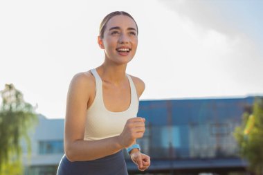 Gülümseyen sporcu kadın antrenman maratonu yapıyor. Güneşli yaz parkında dışarıda antrenman yapıyorum. Sağlıklı yaşam tarzından zevk alan gülümseyen genç bir kız. Kadın atlet koşucu.