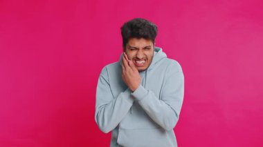 Diş sorunları. Hintli Hintli adam yanağa dokunuyor, korkunç bir ifadeyle gözlerini kapatıyor diş ağrısı, hassas dişler, çürükler yüzünden acı çekiyor. Pembe arka planda izole edilmiş Arap genç adam.