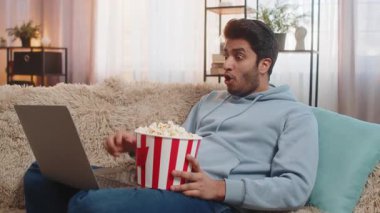 Hintli genç adam patlamış mısır yiyor ve dizüstü bilgisayarda film izliyor, dinlenmenin tadını çıkarıyor. İspanyol adam oturma odasında kanepede oturup gülümserken abur cubur yiyor ve en sevdiği filmle eğleniyor..
