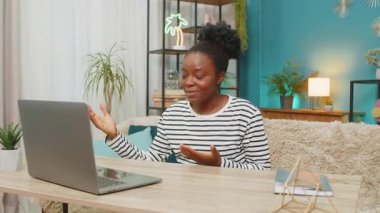 Afro-Amerikalı genç kız evdeki video konferansına katılıyor. Hareketli hareketler, dizüstü bilgisayarda gösteriliyor. Kendine güvenen ifadeler, koltukta oturmak, kapalı mekanlarda online iletişim kurmak.