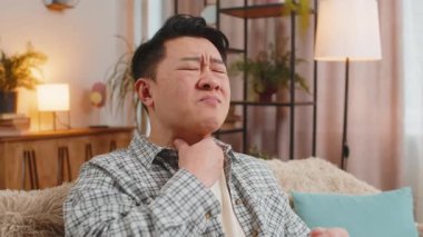 Üzgün Çinli adam boğazı ağrıyan adamın elini tutuyor. Ağrılı boyun ve kaşları çatık, tiroid bozuklukları boğaz ağrısı, bademcik iltihabı. Orta Doğulu genç adam sınıftaki kanepede oturuyor..