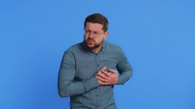 Stresli, orta yaşlı, gözlüklü, orta yaşlı, orta yaşlı, kalp krizi geçirme riski olan, kalp krizi geçiren, kalp krizi geçiren, kötü bir hastalık belirtisi gösteren bir adamdan muzdarip. Mavi arkaplanda izole edilmiş adam.