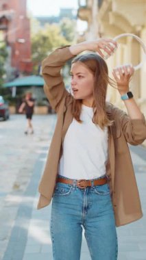 Kablosuz kulaklık takan mutlu beyaz kadın dışarıda dans eden enerjik disko rock 'n roll müziği dinliyor. Şehirli, güneşli sokakta yürüyen genç bir kız. Yaşam Tarzları.