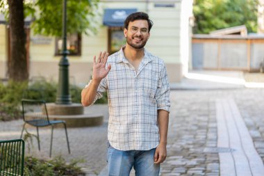 Hoş geldiniz. Hintli genç adam kameraya dostça gülümsüyor, el sallıyor selam veriyor, selamlıyor ya da veda ediyor, dışarıda misafirperver bir ifadeyle karşılıyor. Şehir sokağındaki Arap adam. Yaşam tarzları. Yatay