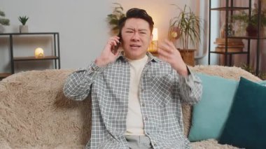 Kızgın genç adam evdeki kanepede otururken akıllı telefonda tartışıyor. Tartışma. Çinli yetişkin bir adam yüksek sesle konuşur ve cep telefonuna bağırır, kötü niyetle el kol hareketleriyle mesaj iletir ve ispatlar..