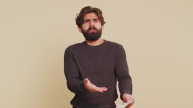 Zavallı Hintli genç adam, yetersiz parasıyla, elinde bir dolar banknot tutuyor. Finansal kriz. İflas. Yoksulluk ve yoksulluk. Yetişkin Lübnanlı Hintli adam bej arka planda duruyor..