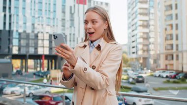 Cep telefonu kullanan Kafkas iş kadınının şehir merkezindeki akıllı telefon bahsini kazanan kadını şaşırtarak zafer başarısını kutlamasına şaşırdım. Şehir sokağında duran kız.