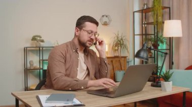 Kulaklık takan genç işadamı, serbest çalışan, çağrı merkezi ya da destek operatörü yardım hattı, müşteri ya da iş arkadaşı iletişim desteği ile konuşuyor. Ofis masasında dizüstü bilgisayar kullanan adam..