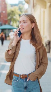 Telefon, iyi haber, dedikodu. Akıllı telefondan hoş sohbetler yapan mutlu beyaz kadın turist, açık havada arkadaşlarıyla konuşmaktan keyif alıyor. Şehir caddesinde yürüyen bir kız. Kasaba yaşam tarzları.