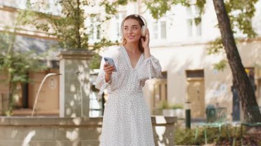 Kablosuz kulaklıklar takmış, açık havada dans eden ve en sevilen disko rock 'n roll müziğini dinleyen mutlu, gevşemiş genç yetişkin kız. Şehir Günışığı Caddesi 'nde duran beyaz kadın..