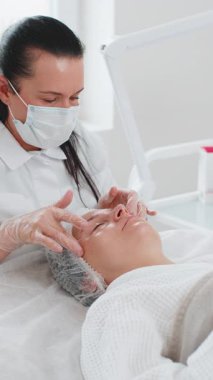 Terapist kadın, elleriyle spa masajı yaptırıyor. Salonda pürüzsüz, sağlıklı cilt bakımı. Göz altı torbaları iyileşiyor. Yüz fizyolojisi seansında müşteri. Dikey çekim