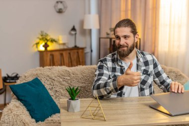 Mutlu gülümseyen genç adam ev masasındaki görevlerini tamamlıyor, bilgisayarını minnettar bir ifadeyle kapatıyor. Kanepede oturan beyaz bir adam kameraya doğru dönüyor, iyi bir iş çıkardığını söylüyor..