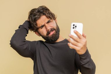 Lübnanlı genç adam cep telefonu daktilo yazarken, şaşırarak aniden piyango sonuçlarını kaybediyor, kötü talih, kayıp, başarısızlık. Yakışıklı Hintli erkek, bej renkli stüdyo arka planında izole edilmiş..