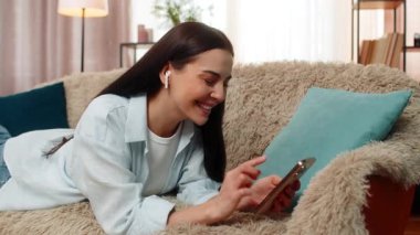 Evde, kulaklık takmış, kanepeye uzanmış genç bir kadın cep telefonuyla sosyal medya yayınını rastgele kaydırıyor. Kafkasyalı kız dinleniyor, çevrimiçi içerikten, müzikten, eğlenceden ve boş zamanlardan keyif alıyor..