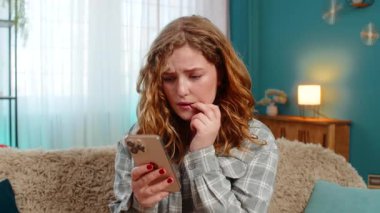 Evde endişeli bir şekilde önemli bir mesaj bekliyor. Akıllı telefonu kaydırırken tırnağını yiyor. Kanepede oturan beyaz saçlı kız gergin, stresli, duygusal beklenti, gerilim anı