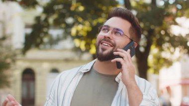 Gözlüklü, gülümseyen cep telefonuyla konuşan beyaz tenli genç adam iyi haberler alıyor. Cep telefonu kullanan adam, şehir caddesinde haber arkadaşlarıyla telefon görüşmelerini tartışıyor.