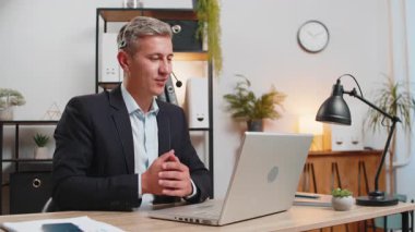 Kulaklık takmış yakışıklı, beyaz, genç bir işadamı bilgisayarla ofis masasında konuşuyor. Erkek danışmanın internet danışmanlığı, müşteri desteği, şikayetleri olan müşterilere yardım.