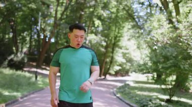 Asyalı koşucu şehir parkında koşuyor ve akıllı adam arıyor. Akıllı bilezik kullanan adam. Zindelik portresi Japon adam sonuçları kontrol ediyor. Spor kıyafetleri içinde yakışıklı bir erkek açık havada koşmaktan hoşlanıyor..