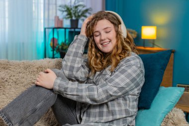 Evde kulaklık takan genç bir kadın. Gözleri kapalı. Nazikçe dans ediyor ve favori müzikten hoşlanıyor. Kafkasyalı kızıl saçlı kız kanepenin üzerinde ritme göre hareket ediyor, neşe, duygusal huzur ve rahatlama hissediyor.