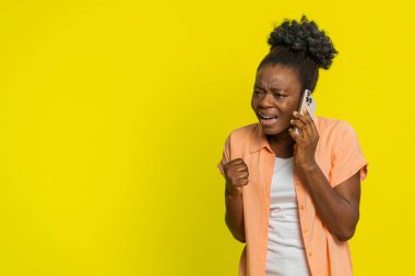 Telefonda konuşan Afro-Amerikalı kadın öfke dolu bir şekilde hayal kırıklığı tatsızlığını dile getiriyor. Siyah kız sarı arka planda izole edildi. Ateşli konuşma sırasında negatif duygular ve gerilim.
