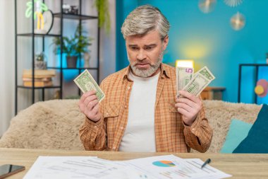 Evdeki masada oturan olgun bir adam, etrafı evrak faturalarıyla çevrili, elinde az miktarda nakit para var. Finansal zorluklar, iflas ve stres yüzünden hayal kırıklığına uğramış bir adam.