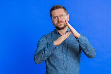 Kafkasyalı orta yaşlı bir adamın mola verme hareketi, sınır veya dur işareti göstermesi, baskı yok, daha fazla zamana ihtiyacım var, dinlenmek, dinlenmek, yardım. Genç yetişkin adam mavi arka planda izole edilmiş