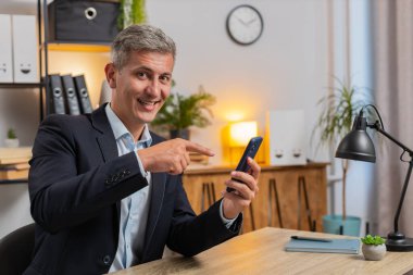 Akıllı telefon uygulamasını kullanarak mobil ekran uygulamasını gösteren kendine güvenen genç bir iş adamı. Ofiste çalışan uzaktan kumandalı bir iş. Kameraya bakan serbest çalışan yakışıklı bir adam. Reklamcılık