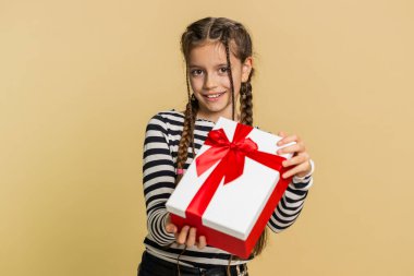 Doğum günü hediye kutusunu sunan, gülümseyen, genç, güzel bir kız çocuk. El uzatıyor, hediye paketi yapıyor, kariyer ikramiyesi teklif ediyor, kutlama partisi veriyor. Stüdyo bej arka planda küçük şirin çocuklar