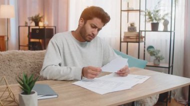 Evrakları tutan ve inceleyen genç Hintli adam, evdeki oturma odasında otururken faturalar ve harcamalar yüzünden hayal kırıklığına uğramış görünüyor. İspanyol adam da evde bunalmış hissediyor..