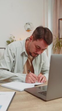 Genç adam video derslerine ya da ofis masasındaki dizüstü bilgisayardaki ofis toplantısına katılırken not alıyor ya da not alıyor. Webcam 'e bakan Serbest Çalışan Destek Servisi.